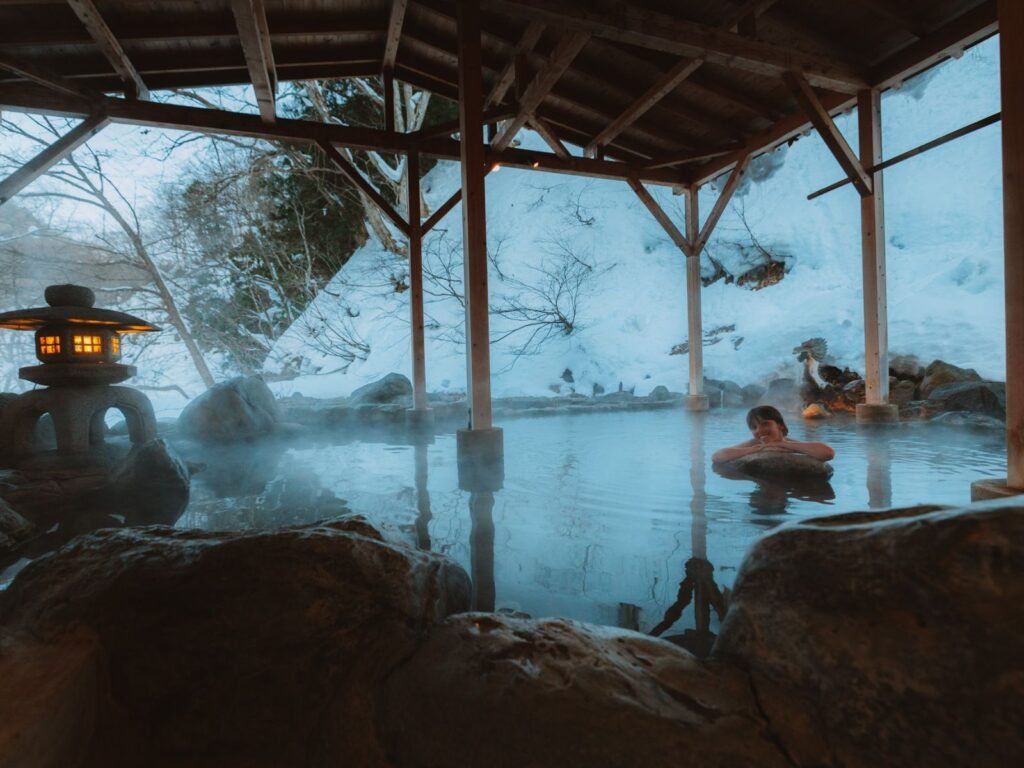 girl relaxing by a rock in the middle of a large-open air private onsen at the onsen theme park in Japan